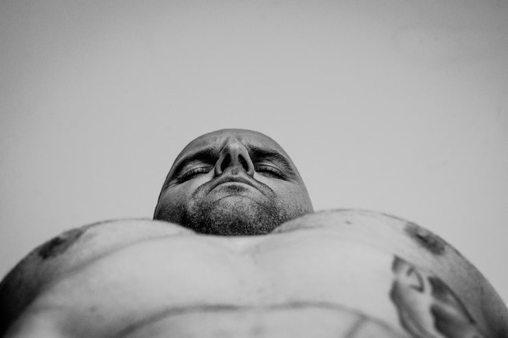 Shirtless man lying against wall